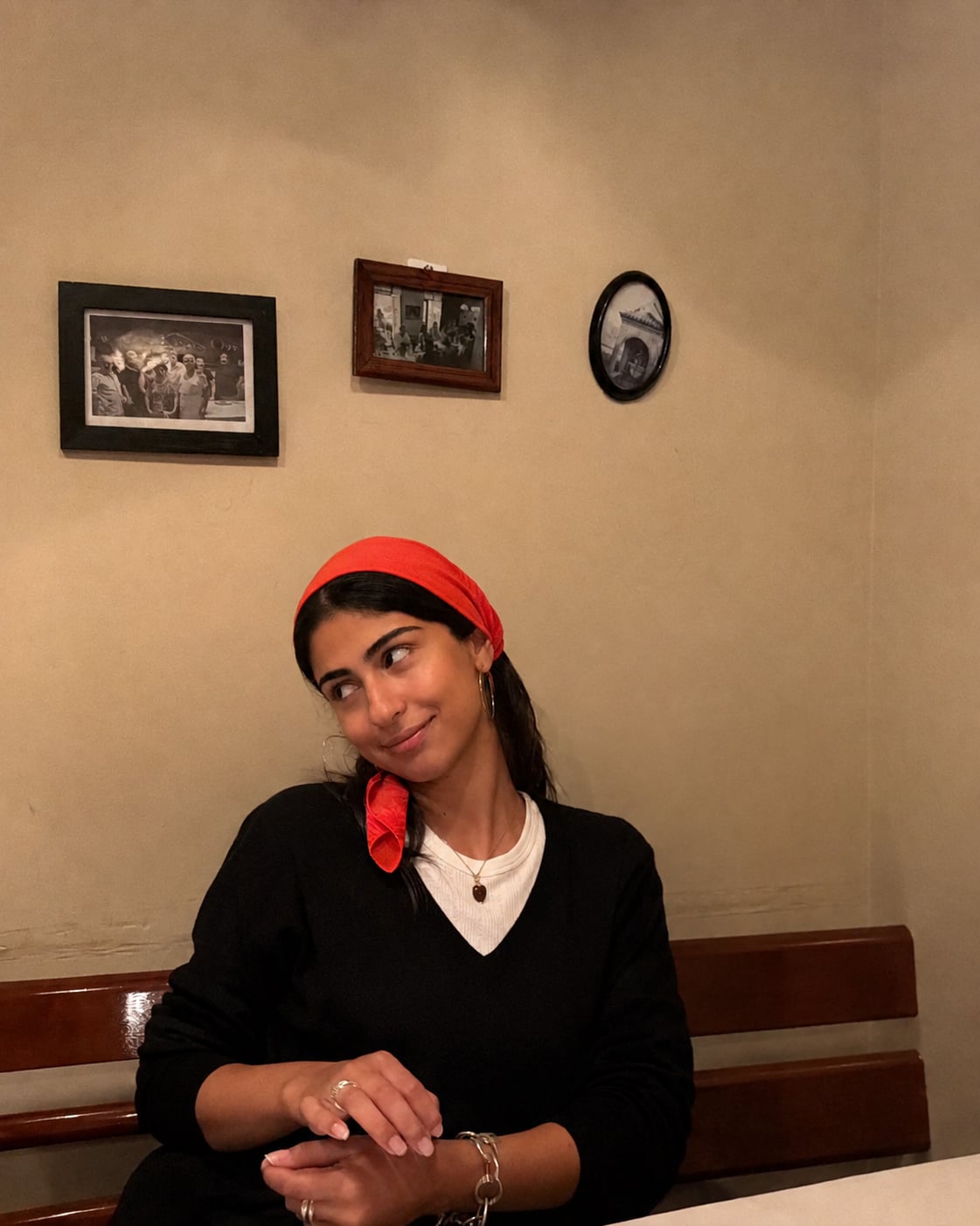Noor Aslani in a red headscarf and black jumper, smiling and looking to the side at a restaurant table